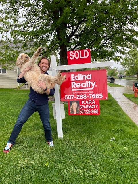 Home buyer standing with dog in front of a sold sign